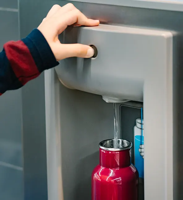 A person using a bottle filling station for schools, to fill their reusable water bottle.