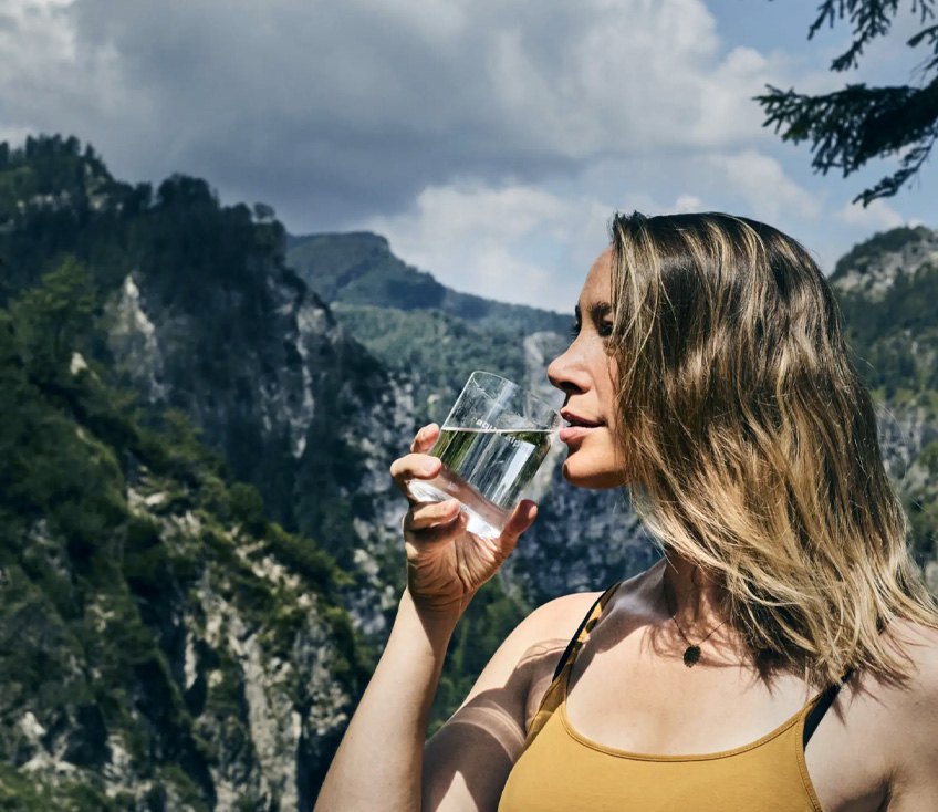 Frau trinkt aus Wasserglas in den Bergen
