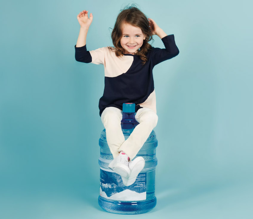 Kind sitzt auf Alpenwasserflasche und freut sich