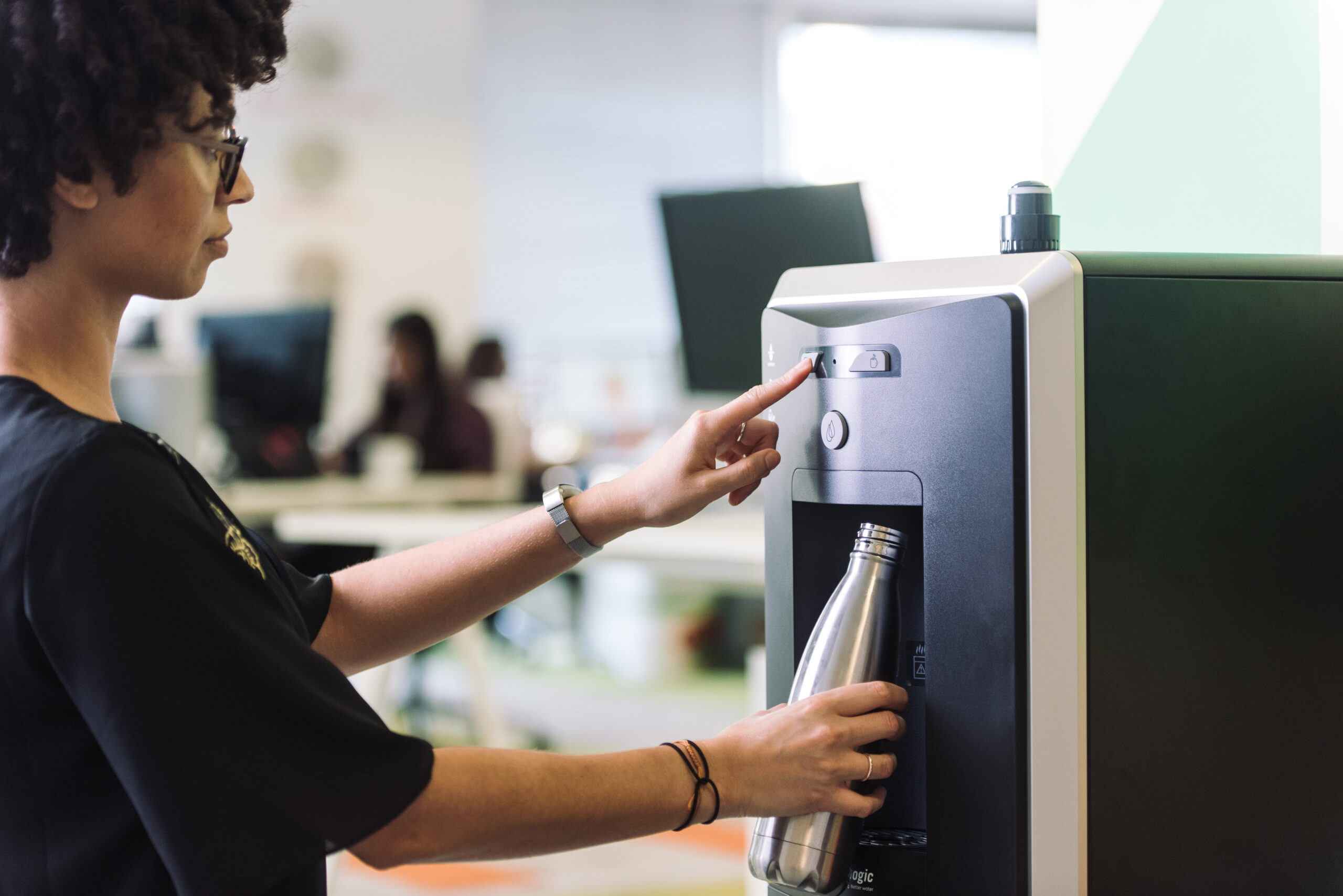 Frau füllt im Büro ihre Mehrweg-Flasche am Culligan Wasserspender auf