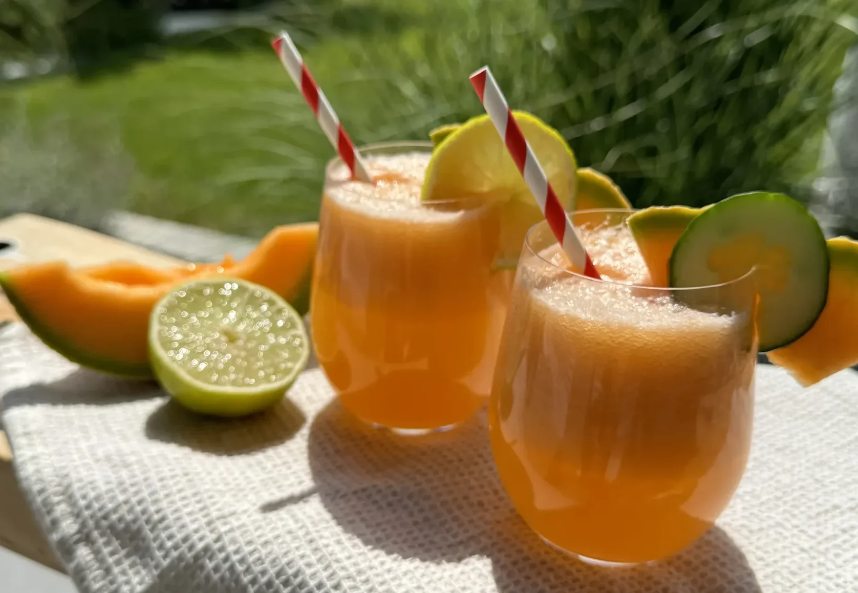 Zuckermelone-Gurke Limonade mit Limette im Glas, serviert mit Strohhalm und frischen Melonenscheiben im Sommergarten.