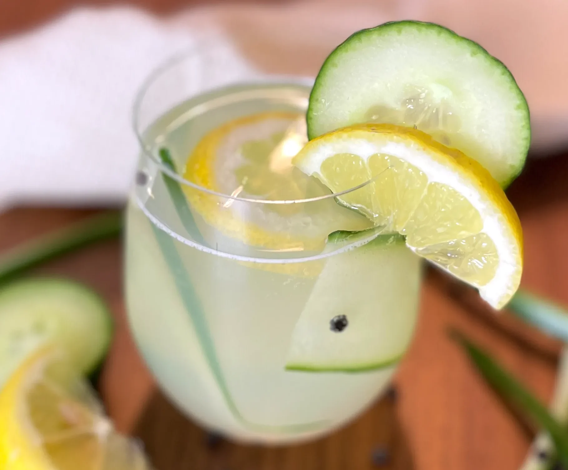 Erfrischender Gin-Tonic-Mocktail mit Zitronen- und Gurkenscheiben sowie Eiswürfeln in einem Glas, dekorativ serviert auf Holzuntergrund mit frischen Zutaten.