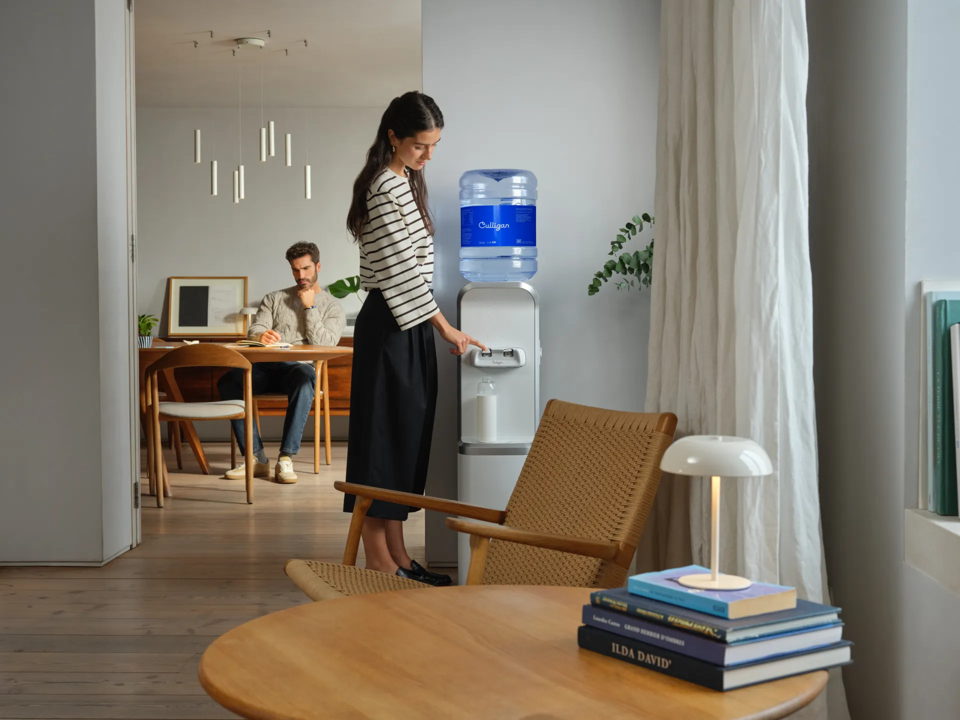 Ein Culligan Wasserspender steht in einem Wohnzimmer. Eine Frau zapft Wasser vom Wasserspender in eine Wasserflasche.
