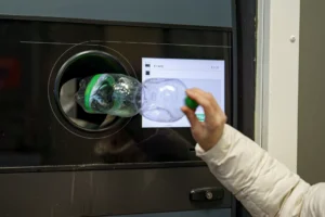 Eine Frauenhand gibt eine Plastikflasche in den Pfandrückgabeautomat